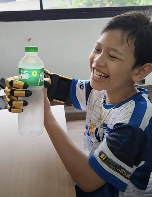 K. grinning as he holds a water bottle with his gold Kinetic Arm