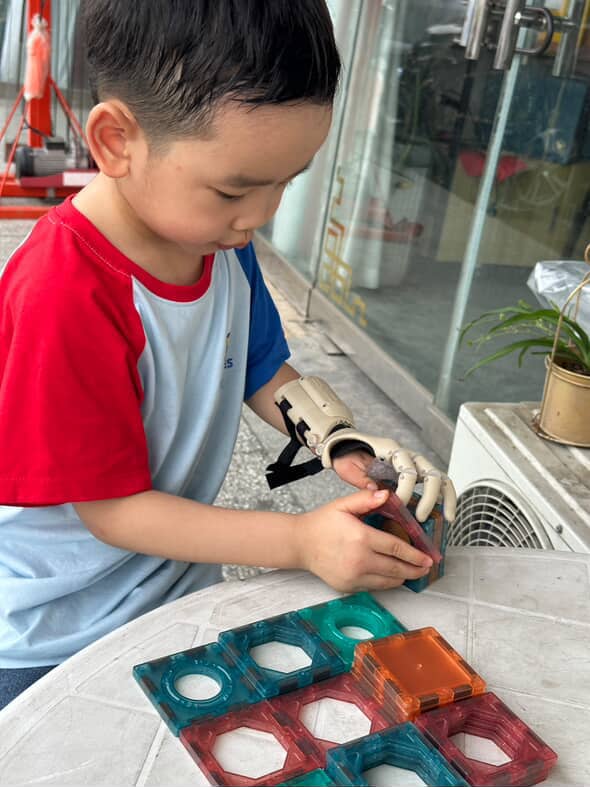W. playing with magnetic building tiles, using arm to grip pieces
