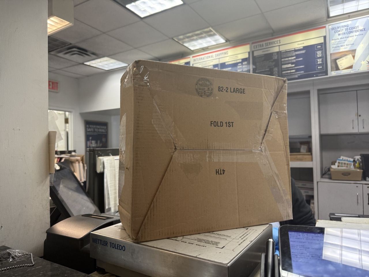 Shipping box on scale at post office counter, addressed to Uganda