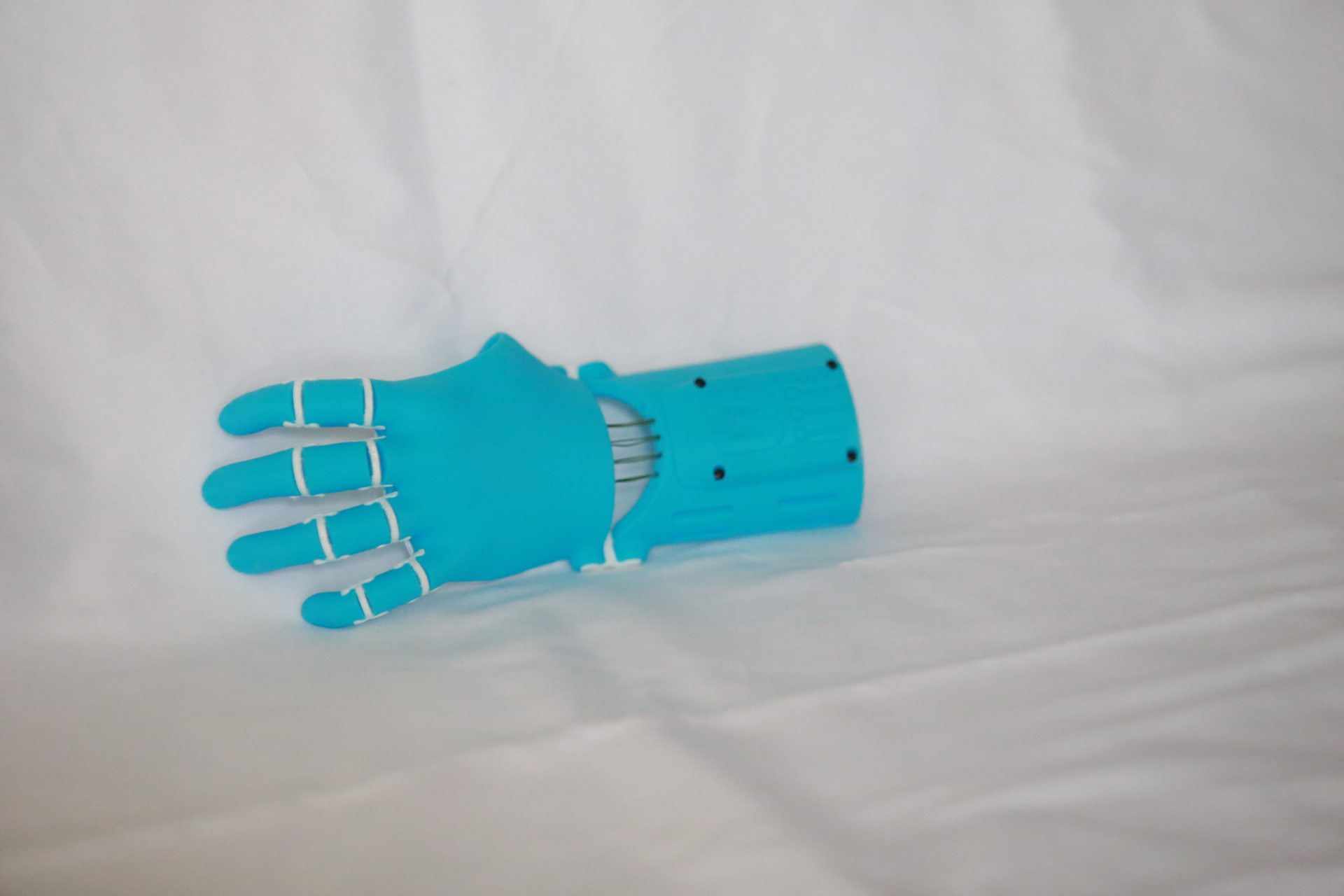 The finished 55% light blue Thumbless Kinetic Hand lying flat on white fabric, fingers extended