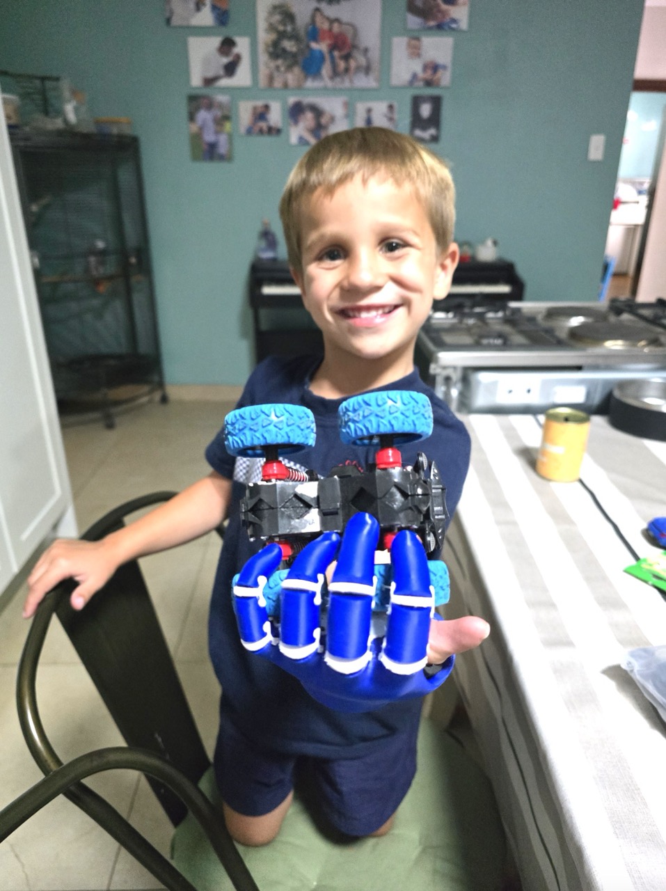 Noah, 4 years old, beaming with a huge grin and holding a toy car gripped in his dark blue prosthetic hand, at home in Strand, South Africa