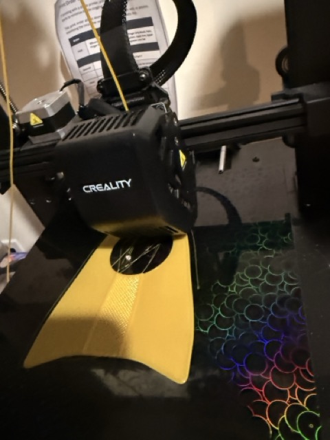 The Creality printer working on a yellow component for O.'s arms, filament visible mid-print
