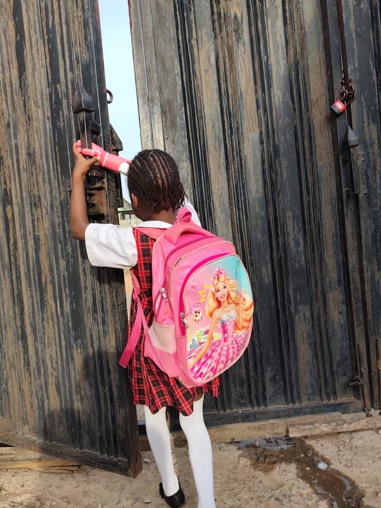 O.C. from behind in school uniform, using her pink prosthetic arm to push open the school gate