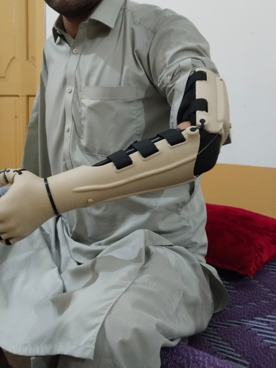 A.S. seated, holding the Kinetic Arm with the right sleeve, close-up on the arm mechanism