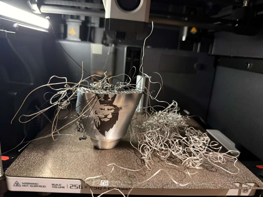 The failed first print: a tangle of silver filament over a partial palm, mid-failure inside the printer