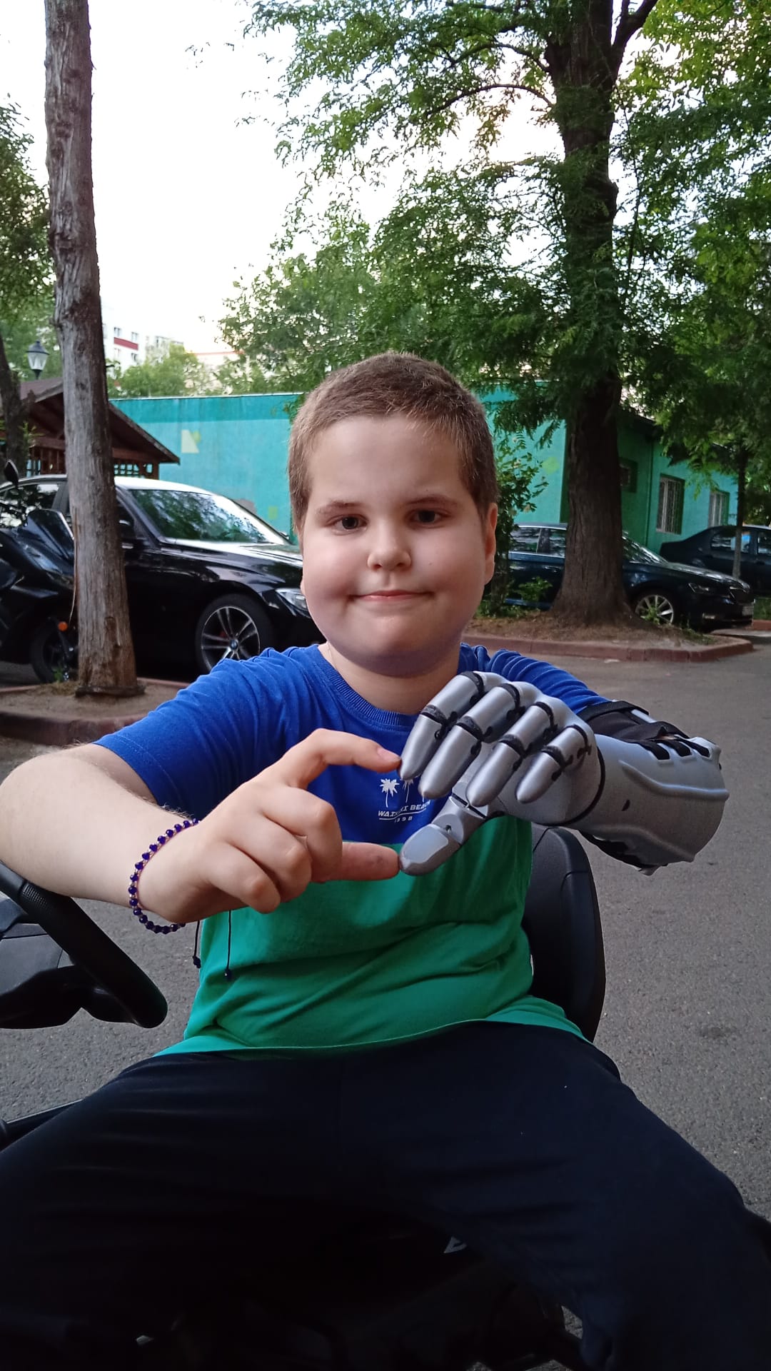 A. sitting in the go-kart seat, showing the silver prosthetic arm toward the camera